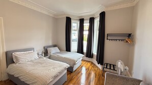 Een slaapkamer met twee bedden, een raam met gordijnen, een ventilator en een plank met handdoeken.