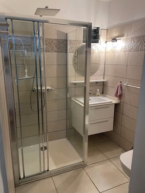 Een moderne badkamer met een glazen douchecabine, een witte wastafel en een spiegel erboven.