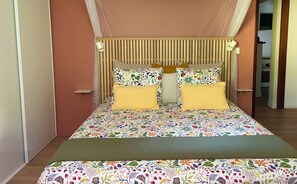 Een bed met een bloemenlaken, twee gele kussens en een houten hoofdbord.