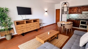 A modern living room with a sofa, coffee table, TV, wooden cabinet, and a dining area with chairs and a table. - Comfortable apartment in a hotel residence, Chill and festive atmosphere (Albufeira)