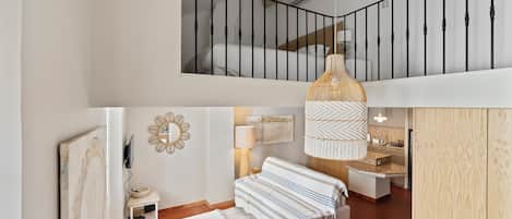 A spacious loft with a high ceiling, a mezzanine bedroom, a dining area, and a kitchen with a view.