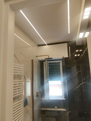 Um banheiro moderno com chuveiro em box de vidro, porta-toalhas branco e parede de mármore.