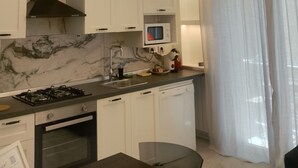 Eine moderne Küche mit weißen Schränken, einem Gasherd, einer Mikrowelle und einem eingebauten Backofen. Ein großes Fenster mit transparenten Vorhängen und eine Deckenleuchte mit geometrischem Design.