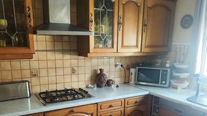 A kitchen with wooden cabinets, a gas stove, a microwave, and a window with curtains. - House for rent near Paris (Livry-Gargan)