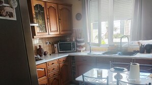 A kitchen with wooden cabinets, a microwave, a sink, and a glass dining table with chairs. - House for rent near Paris (Livry-Gargan)
