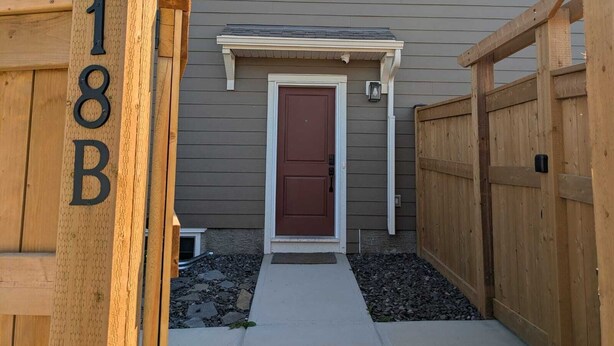 Una casa con una porta marrone, un piccolo portico e una recinzione in legno.