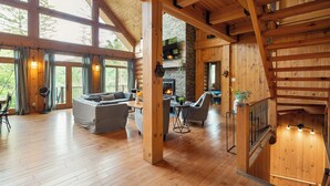 Un interior espacioso de madera con chimenea, ventanas amplias y una escalera.