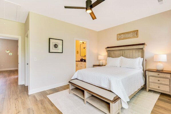 A bedroom with a bed, bedside tables, a ceiling fan, and a bathroom visible through an open door.