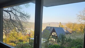 A view from a window overlooking a house with a sloped roof and solar panels, surrounded by trees and a distant town. - Little Rhine View Château - Harry: Apartment at the largest Rhine bend/loop (Boppard)