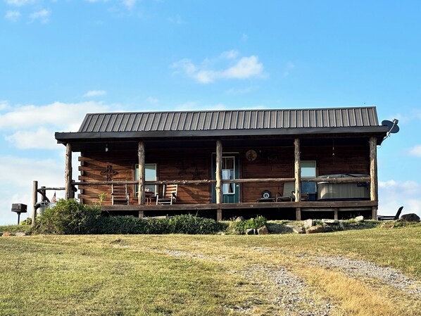 A rustic log cabin with a porch, a satellite dish, and a flag.