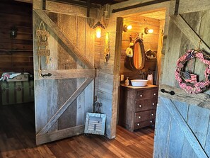 A rustic cabin interior with a wooden door, a small cabinet, a sink, and a mirror.