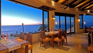 A dining area with a view of the ocean, large windows, and ceiling fans. - Luxe Oceanfront Retreat on Beach, Puerto Vallarta (Puerto Vallarta)