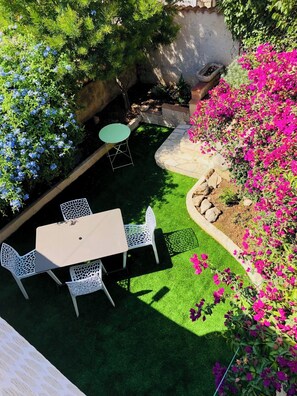 Une terrasse avec une table et des chaises, entourée de pelouse verdoyante et de plantes en fleurs.