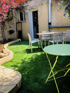 Un espace patio aménagé avec une table et des chaises, un petit parterre et une porte donnant sur un espace abrité.