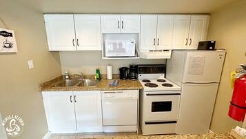 Una cocina compacta con armarios blancos, microondas, estufa y refrigerador.