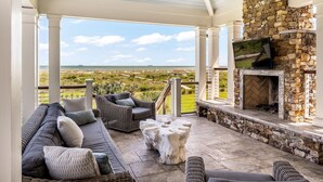 A covered outdoor seating area with a stone fireplace, a television, and a view of the beach.