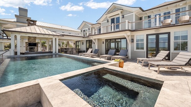 A large outdoor swimming pool with a stone-lined edge, surrounded by lounge chairs and a covered patio area.