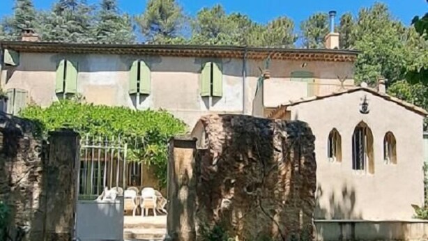 A rustic building with a stone wall, a gate, and a small garden area.