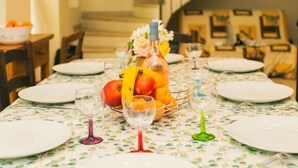 A dining table set with plates, cutlery, and a centerpiece of fruit and flowers.