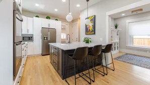 Una cocina moderna con armarios blancos, una isla central con taburetes de bar, electrodomésticos de acero inoxidable e iluminación colgante.