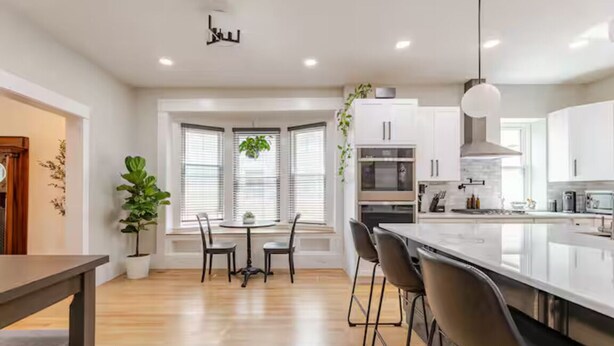 Una cocina moderna con armarios blancos, una isla grande y una zona de comedor con mesa y sillas.