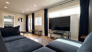 Una sala de estar moderna con un televisor de pantalla plana grande, sofás oscuros y un banco.