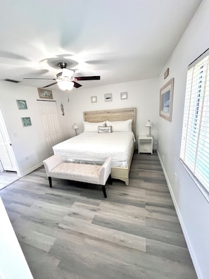 A bedroom with a bed, a bench, a nightstand, a ceiling fan, and a window with blinds.