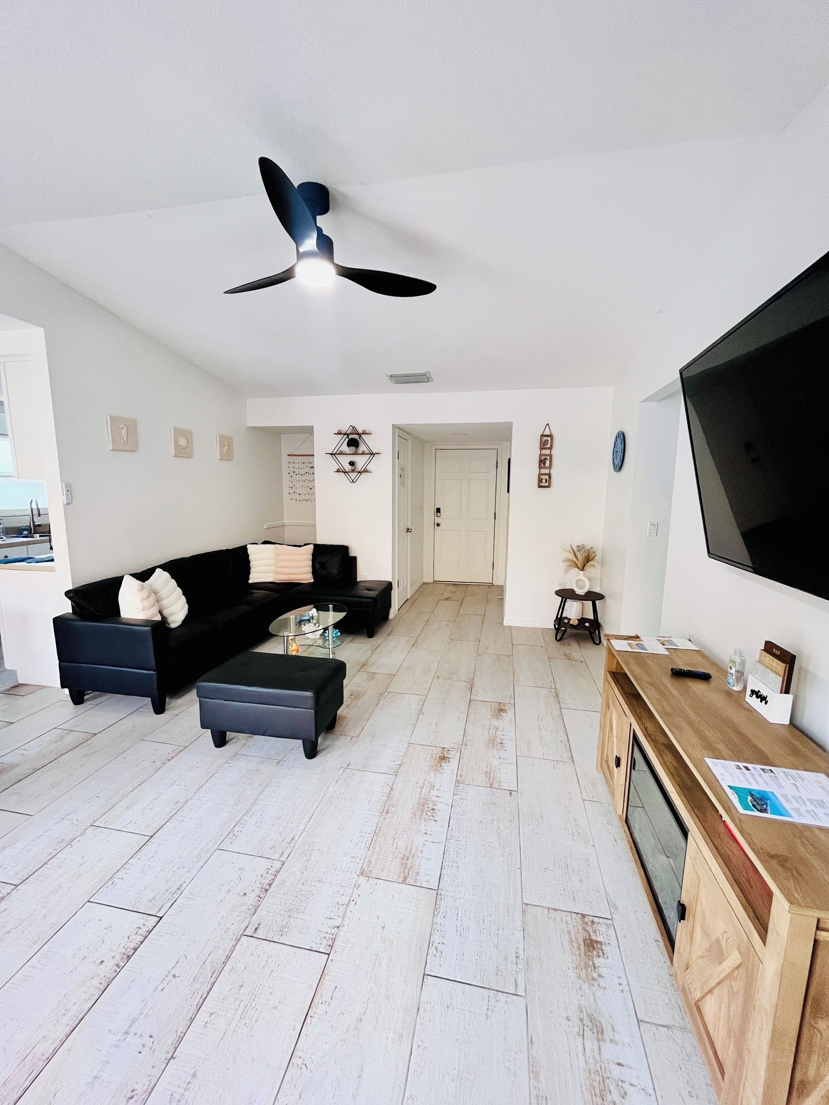 A modern living room with a black sofa, a glass coffee table, and a wooden TV stand.