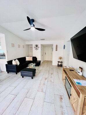 A modern living room with a black sofa, a glass coffee table, and a wooden TV stand.