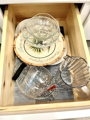 A drawer containing a clear glass bowl, a plate with a floral design, and a silver pitcher.