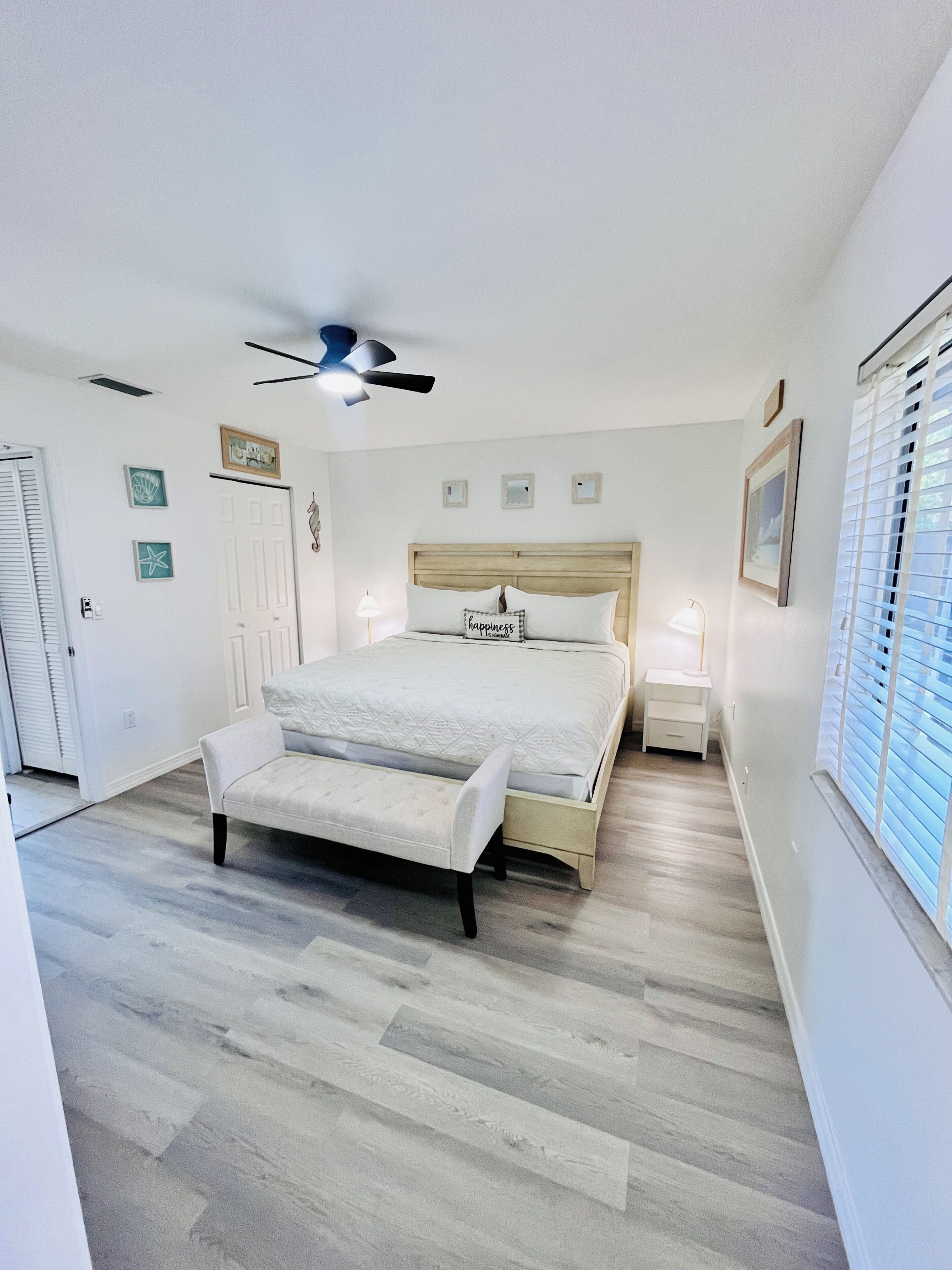 A bedroom with a bed, a bench, a ceiling fan, and a window with blinds.