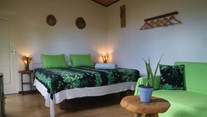 A bedroom with a bed, bedside lamps, a green sofa, a small table, and a potted plant. - Fare atihau vairao  (Taiarapu-Ouest)