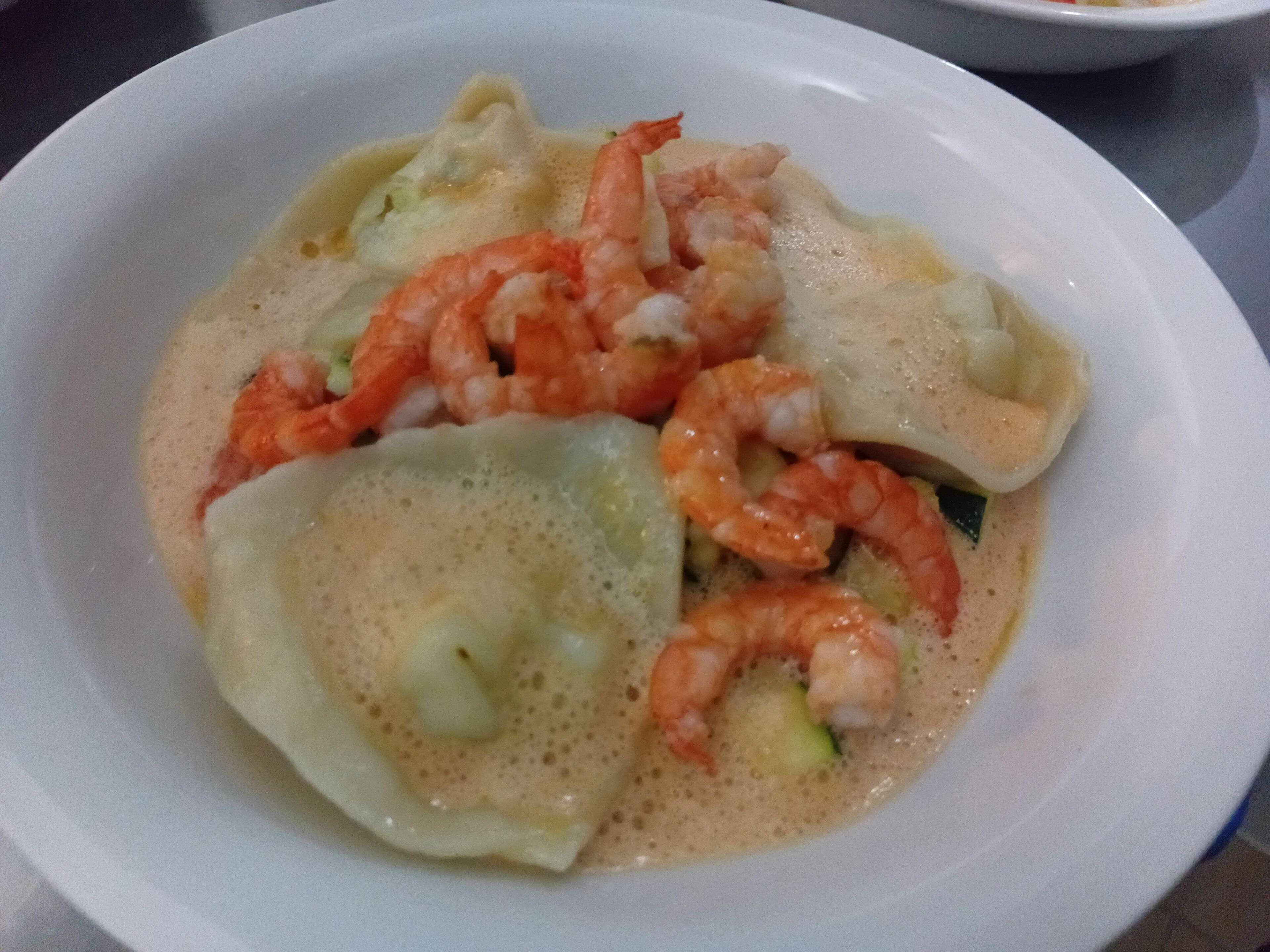 A bowl of soup with dumplings and shrimp.
