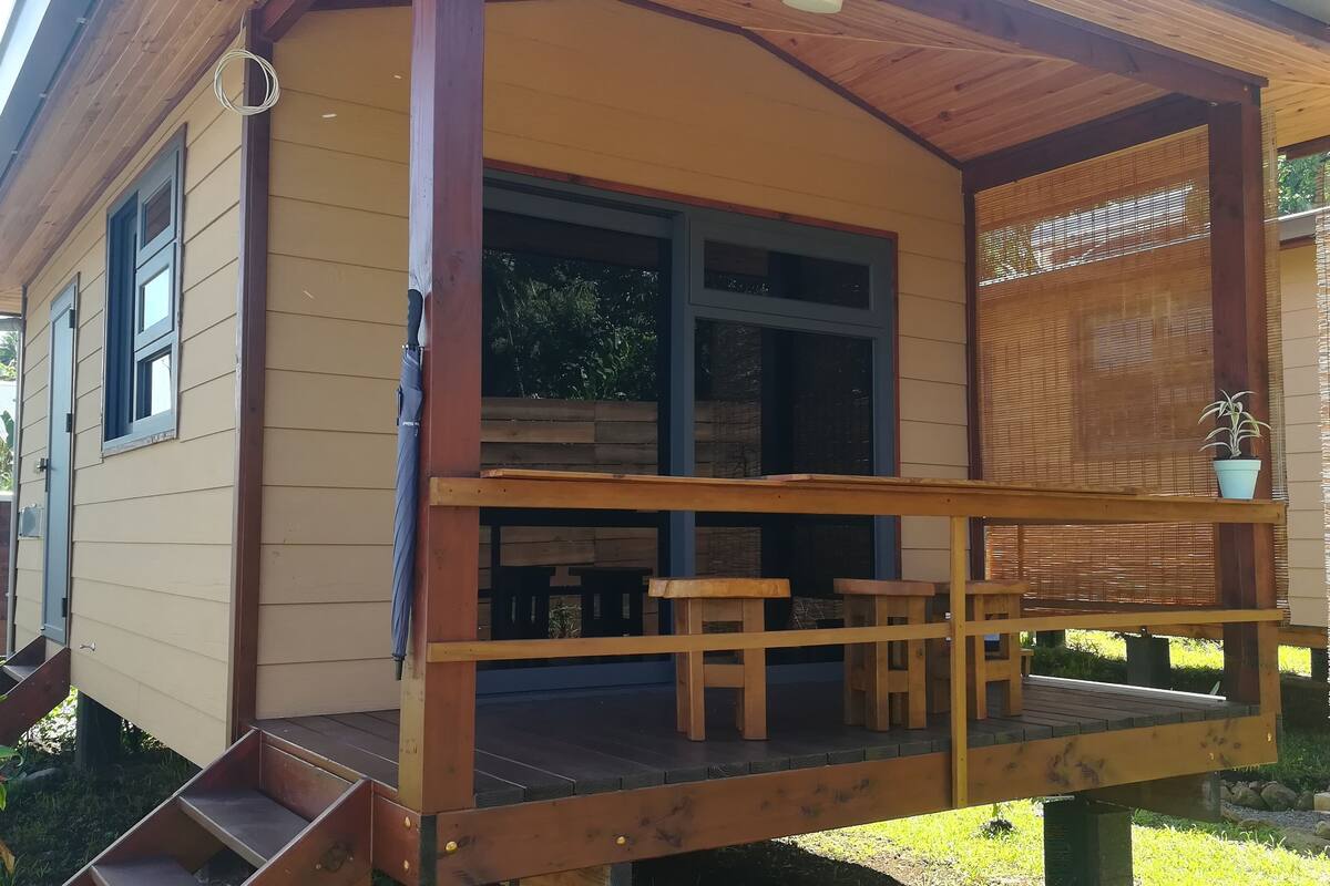 A wooden house with a porch, a small deck, and a potted plant.