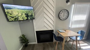 Moderni olohuone, jossa on takka, seinälle asennettu televisio, ruokapöytä tuoleineen ja suuri seinäkello.
