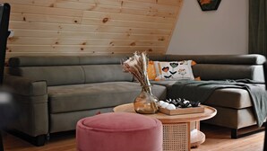 A modern living room with a grey sofa, a small round wooden table with a vase and decorative items, and a pink ottoman. - Cozy A-Frame Cottage, Peaceful Location, HOT TUB, Fire Pit, King Bed, Near Dells (Friendship)
