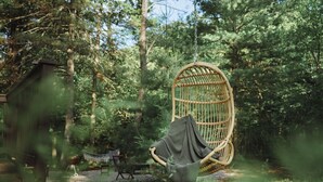 A wicker hanging chair in a forested area with a hammock and a grill. - Cozy A-Frame Cottage, Peaceful Location, HOT TUB, Fire Pit, King Bed, Near Dells (Friendship)