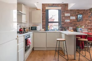 A kitchen with white cabinets, a microwave, a sink, and stools.