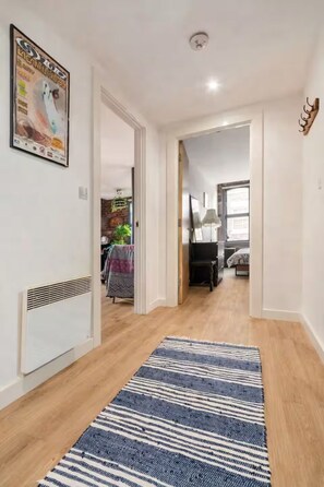 A hallway with a striped rug, a ceiling light, and a poster on the wall.