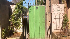 A green gate with a metal arch, a brick building, and a tree with green leaves. - Pet-Friendly, Charming bungalow with WiFi and AC in sunny Yuma (Yuma)