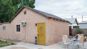 A single-story building with a yellow door, a small window, and a patio area with a table and chairs. - Pet-Friendly, Charming bungalow with WiFi and AC in sunny Yuma (Yuma)