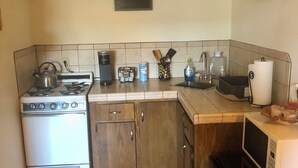 A compact kitchen with a stove, oven, microwave, and refrigerator. There is a sign on the wall, a sink, and various kitchen utensils and appliances. - Pet-Friendly, Charming bungalow with WiFi and AC in sunny Yuma (Yuma)