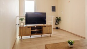 Un salon avec un téléviseur à écran plat posé sur un meuble en bois, une porte blanche et une plante en pot.