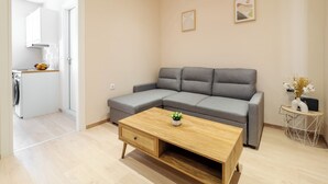 Un salon moderne avec un canapé d’angle gris, une table basse en bois agrémentée d’une plante et une petite table d’appoint avec un vase.