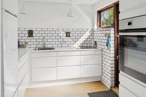 A modern kitchen with white cabinets, a built-in oven, and a window above the sink. - Cozy cottage near beach and nature (Fejø)