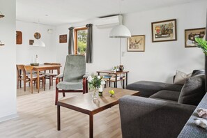A modern living room with a grey sofa, wooden coffee table, and a dining area with wooden chairs and a table.