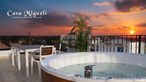 Un jacuzzi en una terraza en la azotea con vistas al atardecer, una mesa y sillas.