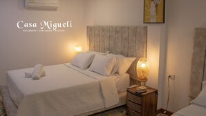 Una habitación de hotel con cama, lámparas de noche, aire acondicionado instalado en la pared y un cuadro.