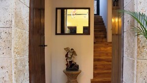 Un pasillo con pared de piedra, una puerta de madera, una pequeña mesa con una escultura y una escalera que sube.