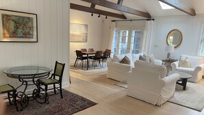 A spacious living room with a round glass table, two white sofas, and a dining area with chairs. - 4-bedroom house in charming Wainscott walking distance to the beach (East Hampton)